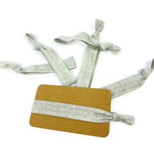 May include: A set of silver glitter hair ties on a brown card. The hair ties are made of elastic and have a knotted design.