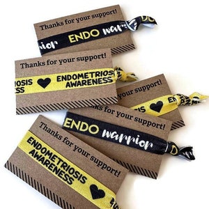 May include: Five brown cards with black and white striped borders and the text "Thanks for your support!" printed on them. Each card has a yellow and black elastic hair tie with the text "ENDO warrior" or "ENDOMETRIOSIS AWARENESS" printed on it.