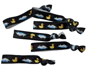 Könnte beinhalten: Ein Set mit fünf schwarzen Gummibändern für Haare mit einem sich wiederholenden Muster aus gelben Gummibärchen und blauen Wellen.