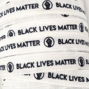 Op de afbeelding: Wit lint met de zin "Black Lives Matter" herhaald en een symbool van een opgeheven vuist in een cirkel.