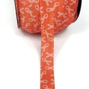 May include: An orange ribbon roll featuring a repeating pattern of white awareness ribbons. The ribbon is made of a woven material and is unrolled, displaying the pattern. Suitable for crafts and decorations.