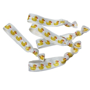 Pode incluir: Um conjunto de quatro elásticos de cabelo brancos com um padrão de patinhos de borracha amarelos.