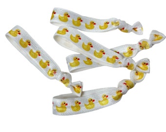 Könnte beinhalten: Ein Set mit vier weißen Gummibändern für Haare mit einem gelben Gummiente-Muster.