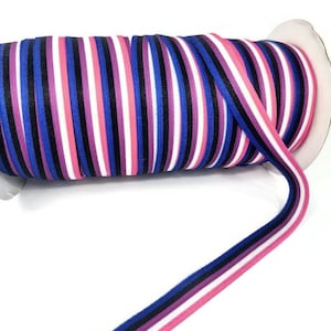 May include: A spool of multi-colored striped ribbon with alternating stripes of pink, white, black, purple, and blue. The ribbon is wound around a white spool.