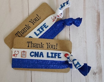 May include: Two blue and white elastic hair ties with the text "CNA LIFE" and a stethoscope and clipboard graphic. The hair ties are on a brown card with the text "Thank You!" printed on it.