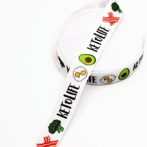 May include: White elastic ribbon with a repeating pattern of avocado, egg, bacon, and broccoli with the text "Keto Life" printed on it.