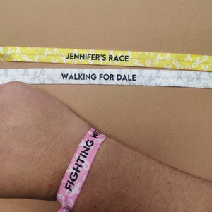 May include: Three pink, yellow, and white wristbands with the text "Jennifer's Race", "Walking for Dale", and "Fighting With" printed on them.