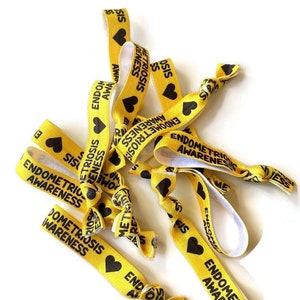 May include: A pile of yellow elastic hair ties with black hearts and the text "Endometriosis Awareness" printed on them.