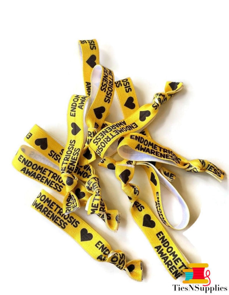 May include: A pile of yellow elastic hair ties with black hearts and the text "Endometriosis Awareness" printed on them.
