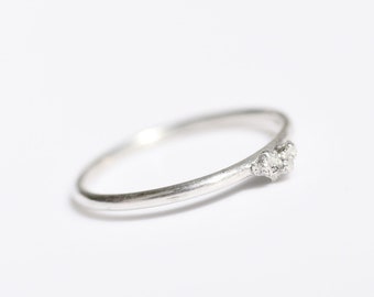 Op de afbeelding: Een sierlijke zilveren ring met een gebogen band en drie kleine, sprankelende edelstenen. De ring is geplaatst tegen een heldere witte achtergrond, wat het elegante ontwerp benadrukt.