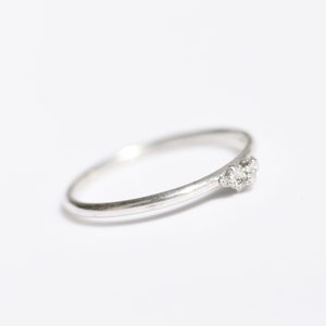 Può includere: Un delicato anello d'argento con una fascia curva e tre piccole gemme scintillanti. L'anello è presentato su uno sfondo bianco pulito, evidenziando il suo design elegante.