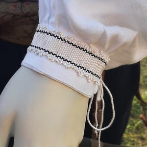Op de afbeelding: Wit overhemd met een zwart-wit geweven manchetdetail. De manchet heeft een decoratieve kantversiering en een witte strik.