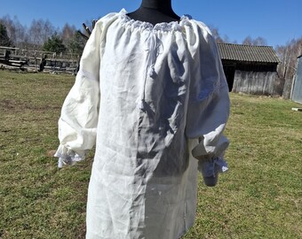May include: A white linen shirt with a lace trim around the neckline and cuffs. The shirt has a gathered neckline and a tie at the front.