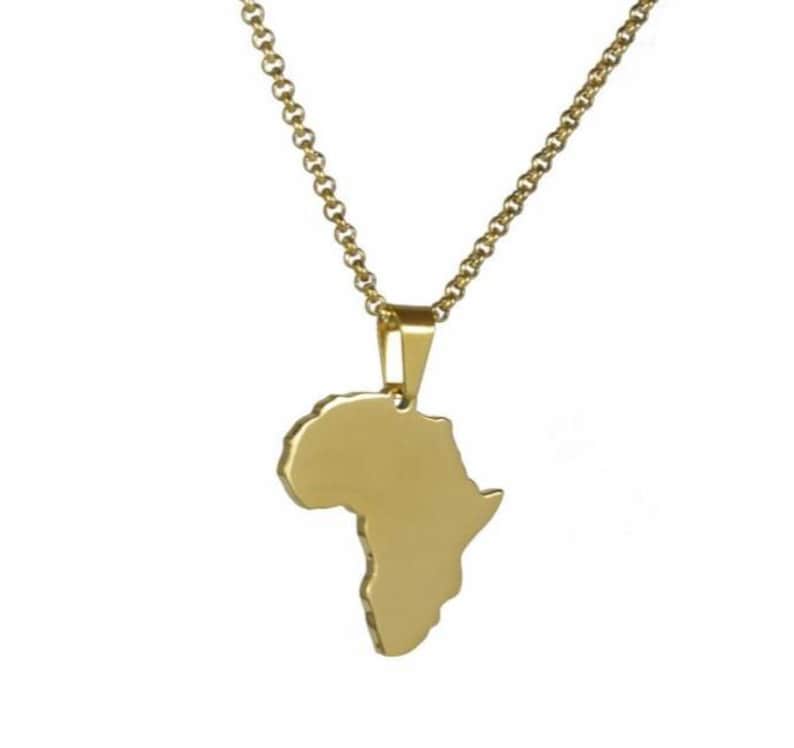 May include: A gold-coloured necklace featuring a pendant shaped like the continent of Africa. The pendant is suspended from a matching gold-coloured chain with rounded links. The surface of the pendant is smooth and solid, reflecting light evenly.