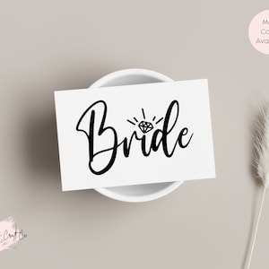 May include: White card with black text that says "Bride" with a diamond ring graphic above the word.