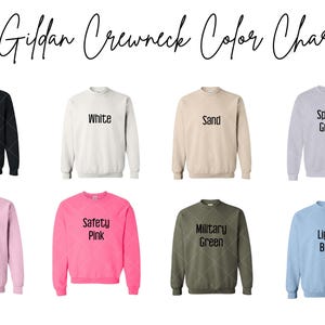 May include: A color chart of Gildan crewneck sweatshirts. The chart displays eight different colors: black, white, sand, sport gray, light pink, safety pink, military green, and light blue. Each sweatshirt has the color name printed on it.