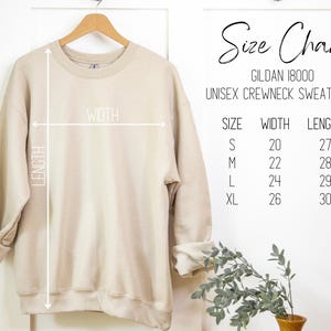 May include: A beige Gildan 18000 unisex crewneck sweatshirt hanging on a wooden hanger. The image includes a size chart with measurements in inches: S (20x27), M (22x28), L (24x29), XL (26x30). The words "Size Chart" are written in cursive.