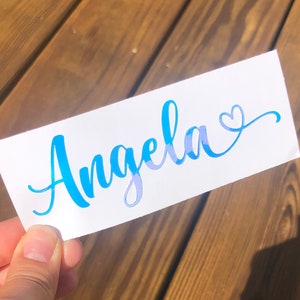 May include: A white sticker with the name "Angela" written in blue cursive lettering with a small heart at the end.