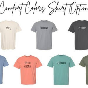 May include: A display of Comfort Colors t-shirts in various colors, including ivory, granite, pepper, washed denim, terracotta, seafoam, and moss. Each shirt has its color name printed on it in a simple font.