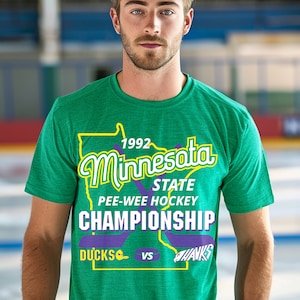 May include: A green t-shirt with a purple outline of the state of Minnesota. The text "1992 Minnesota State Pee-Wee Hockey Championship Ducks vs Hawks" is printed on the shirt.