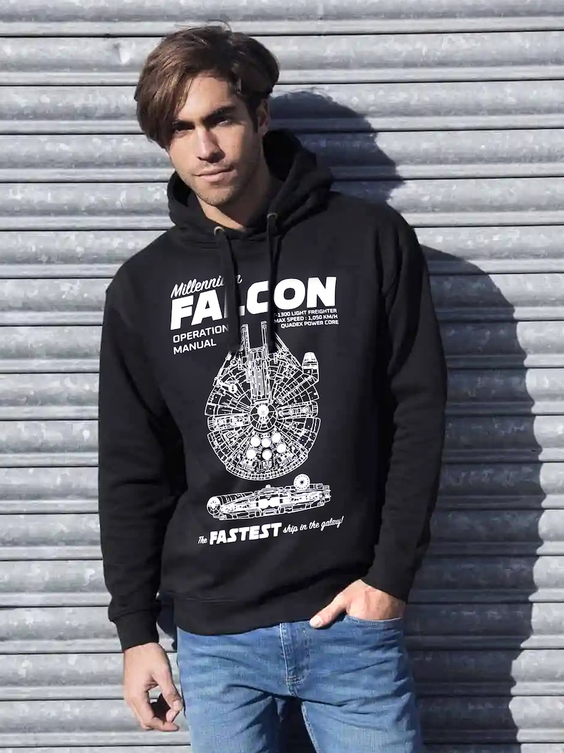 May include: Black hooded sweatshirt with a white graphic of the Millennium Falcon spaceship from Star Wars. The text "Millennium Falcon Operation Manual" and "The Fastest ship in the galaxy!" is printed on the sweatshirt.