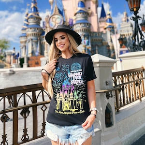 Könnte beinhalten: Ein schwarzes T-Shirt mit einem bunten Motiv von Cinderellas Schloss und Feuerwerk. Der Text "Happily Ever After" ist auf dem Shirt aufgedruckt. Das Shirt trägt außerdem den Schriftzug "The Most Magical Place on Earth".