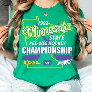 May include: Green t-shirt with a graphic of the state of Minnesota, the text "1992 Minnesota State Pee-Wee Hockey Championship", and the words "Ducks" and "Hawks" with hockey stick graphics.