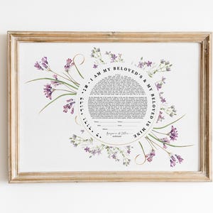 Op de afbeelding: Een rechthoekige ingelijste print met een centraal cirkelvormig tekstblok met Hebreeuwse en Engelse huwelijksgeloften, omringd door aquarelillustraties van paarse bloemen. De tekst luidt I AM MY BELOVED'S & MY BELOVED IS MINE.