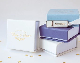May include: A stack of small, book-shaped boxes in white, periwinkle, and light blue, with a USB drive on top. The USB drive is silver with the word "MEMORIES" printed on it. The white box has gold text that reads "Alise & Chris" and the date "September 11, 2021".