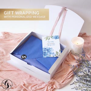 May include: A white gift box with a pink ribbon, containing blue tissue paper secured with a black sticker. A card with blue hydrangea illustrations and the text "Dear Emily, Happy 25th Birthday! Love you, mom" is included. Text reads: GIFT WRAPPING WITH PERSONALIZED MESSAGE.