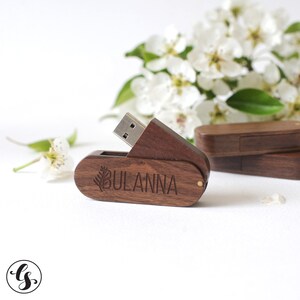 Puede incluir: Una memoria USB de madera con un dise&ntilde;o de hoja y el nombre "BULANNA" grabado en ella. La unidad est&aacute; abierta y el conector USB es visible.