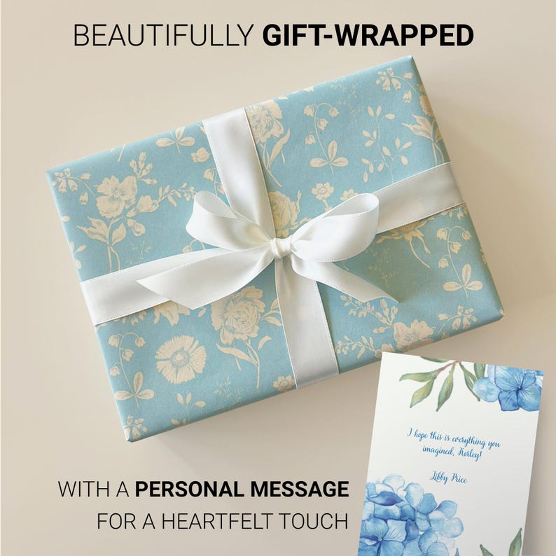 May include: A blue gift box with a white ribbon and a floral pattern. The box is tied with a white bow. A card with a blue floral design and a handwritten message is next to the box. The message reads, "I hope this is everything you imagined, Harley! Libby Price."