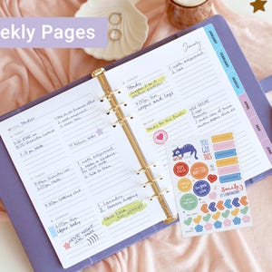 May include: A lavender six-ring binder planner open to a weekly schedule page with handwritten notes, a gold metal pen, and a sheet of colorful stickers featuring various shapes and phrases like You Got This and Smile It's Contagious.