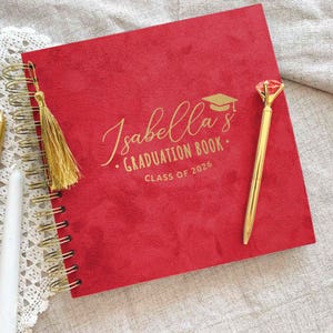 May include: A red graduation book with gold spiral binding, a gold tassel, and a gold pen. The cover features the name "Isabella's" in gold script, along with "Graduation Book" and "Class of 2026".