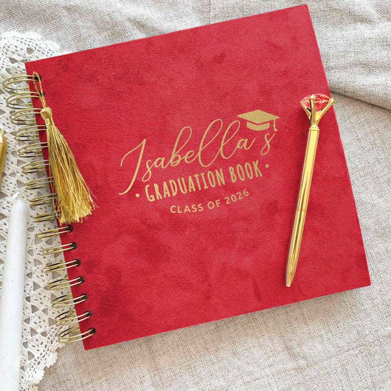 May include: A red graduation book with gold spiral binding, a gold tassel, and a gold pen. The cover features the name "Isabella's" in gold script, along with "Graduation Book" and "Class of 2026".