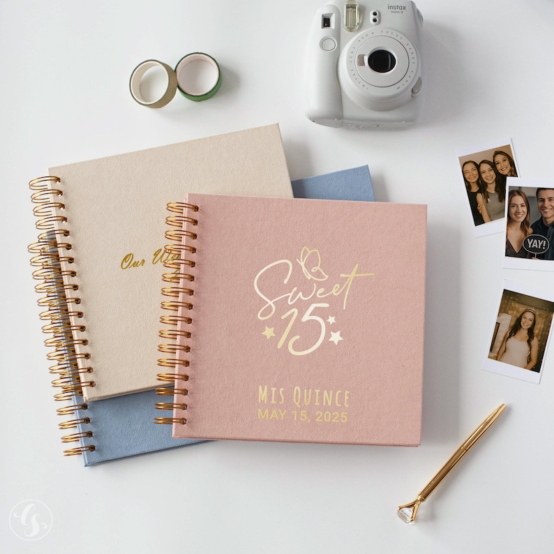 May include: A collection of items including a pink "Sweet 15" journal, a beige journal, a white instant camera, photos, washi tape, and a gold pen with a diamond-shaped top. The pink journal has gold lettering and the date "May 15, 2025".