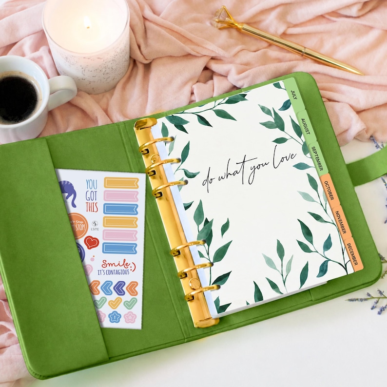 May include: A green ring-bound planner with gold hardware, featuring a white page with green leaf illustrations and the text "do what you love". A sticker sheet with various colorful icons and the text "YOU GOT THIS" and "Smile, IT'S CONTAGIOUS" is tucked into the inside cover.