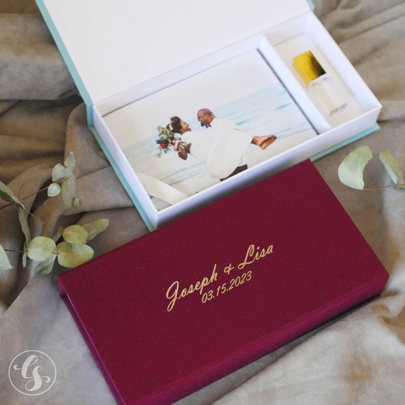 May include: A burgundy velvet box with gold lettering that reads "Joseph & Lisa 03.15.2023". The box is open and contains a white box with a photo of a couple and a small bottle.