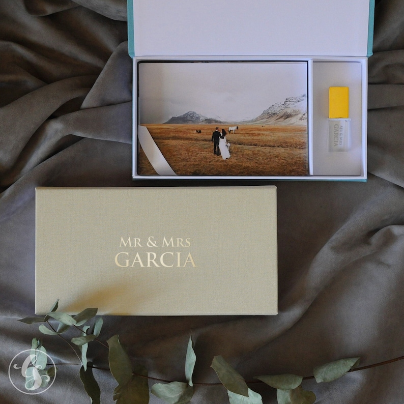 May include: A beige box with the text "MR & MRS GARCIA" in gold lettering. The box is open, revealing a white box with a photo of a couple standing in a field. A small yellow box with a white label is also visible.