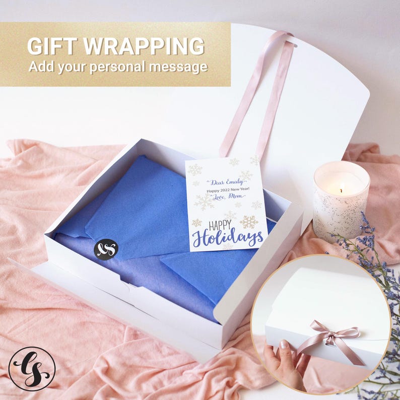 May include: A white gift box containing blue tissue paper, a black circular sticker with white letters, and a white card with gold snowflakes and the text "Dear Emily, Happy 2022 New Year! Love, Mom" and "HAPPY Holidays" in blue script.