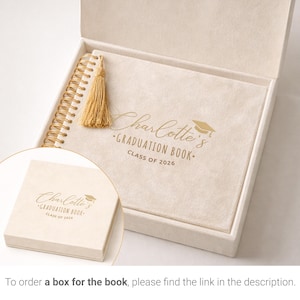 May include: A graduation book in a cream-colored box. The book has a gold spiral binding and a gold tassel. The cover reads "Charlotte's Graduation Book Class of 2026" in gold lettering. A smaller box with the same text is in the foreground.