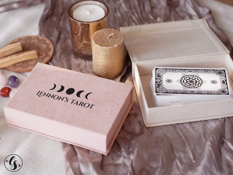 May include: A pink box with the text "Lennon's Tarot" and a moon symbol. The box is open and shows a deck of tarot cards in a white box.