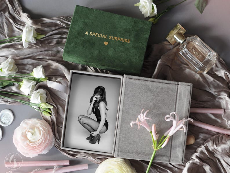 K&ouml;nnte beinhalten: Eine gr&uuml;ne Samtbox mit dem goldenen Text "A SPECIAL SURPRISE" und einem Herz. Die Box ist ge&ouml;ffnet und zeigt ein Schwarz-Wei&szlig;-Foto einer Person. Das Foto befindet sich in einer grauen Box. Blumen und Parf&uuml;m sind ebenfalls im Bild.
