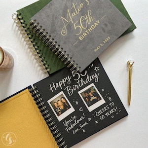 May include: A collection of spiral-bound notebooks with gold accents. One notebook is gray with "Mateo's 50th Birthday" in gold lettering. Another is black with "Happy 50th Birthday" and photos. A gold pen with a diamond-shaped top is also present.