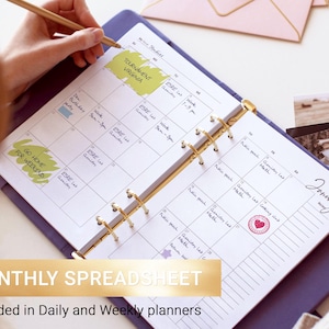 May include: A purple ring-bound planner open to a January monthly calendar page with handwritten notes, yellow highlighter marks, and a red heart stamp. The planner features gold-toned metal rings and white paper with black grid lines and text.