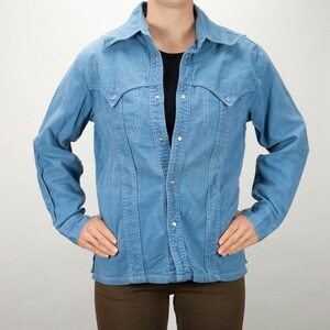Peut inclure: Une chemise en jean bleu clair à boutons et manches longues. La chemise a un style western classique avec deux poches à rabat sur la poitrine.