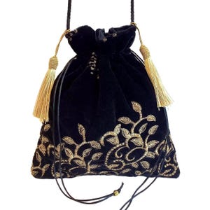 May include: A black velvet drawstring pouch featuring gold metallic thread embroidery in a scrolling leaf and vine pattern along the bottom. The bag includes two long black cord straps and two decorative gold-colored tassels at the top closure.