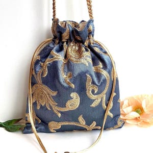 May include: A blue drawstring bag with gold embroidered floral patterns. The bag has a gold cord handle and a gold lining. The bag is made of a soft, textured fabric and is decorated with intricate gold embroidery.