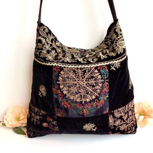 May include: Black velvet shoulder bag with detailed gold embroidery and colourful floral accents. The bag has a long strap and a patchwork design with a central embroidered medallion. A stylish accessory.