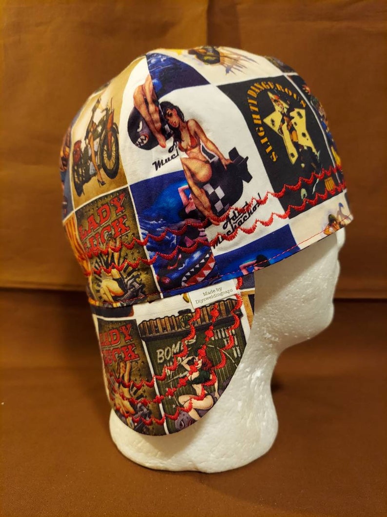 May include: A patchwork welding cap featuring vintage-style pin-up girl and motorcycle graphics in a collage design. The cap has a red embroidered trim and a white interior. The cap is designed to protect the wearer from sparks and heat.